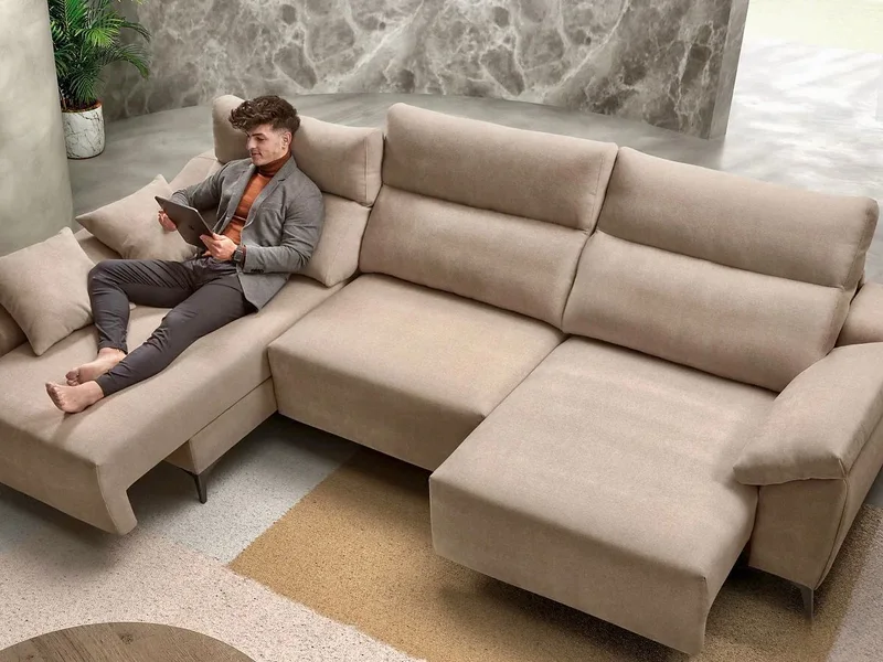 Sofá rinconera beige con chaise longue y asientos deslizantes, con una persona sentada leyendo.