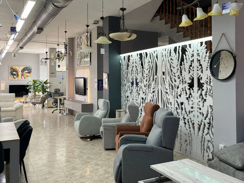 Interior de una de las plantas de exposición: sillones relax tapizados frente a un panel decorativo calado, con lámparas colgantes y la zona de comedores al fondo.