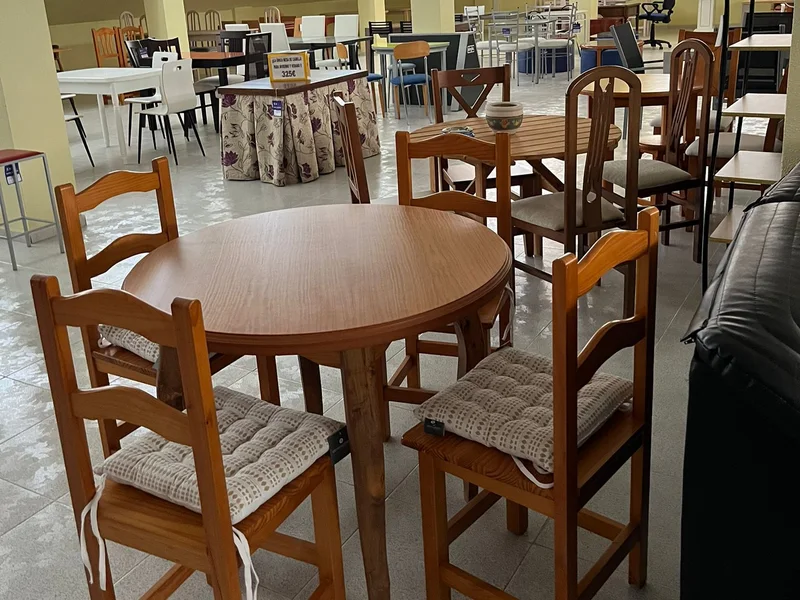 Zona de comedores con mesas de madera redondas y rectangulares y sillas de distintos modelos.
